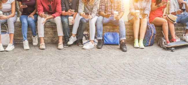 Young friends using smartphones and drinking coffee