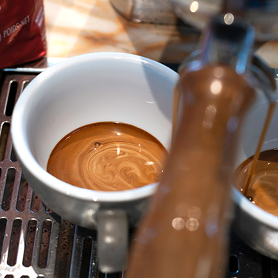 Espresso fließt aus dem Siebträger. Marmorierte Crema sammelt sich am Boden der Espressotasse