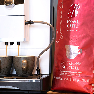 Espresso fließt aus Kaffeevollautomat in zwei Espressotassen. Daneben rote Verpackung Essse Selezione Speciale